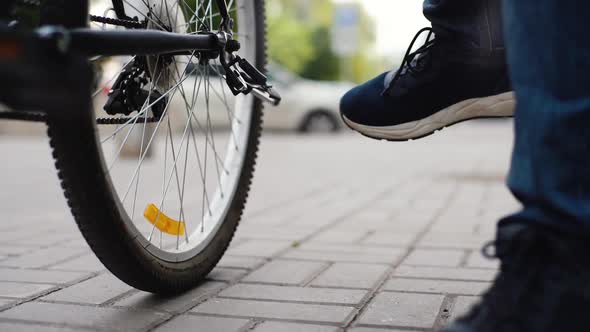Closeup Legs of Unrecognizable Cyclist Male Putting Bike on Footrest on City Street Blurred alt