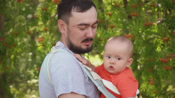 Dad walks with a newborn baby in the park, a child in a sling - a special carrying bag for children alt