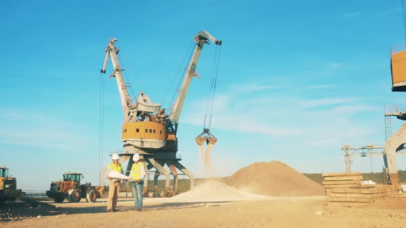 Port Cranes Are Unloading Rubble with Two Engineers Talking Nearby alt