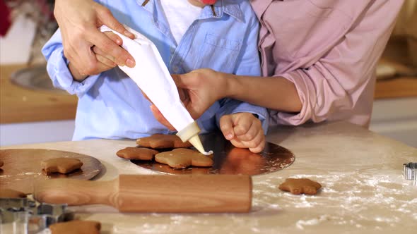 Mother with Son is Decorates a Christmas Gingerbread Cookies with Pastry Bag alt