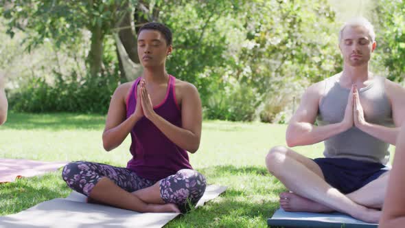 Group of diverse young people meditating and practicing yoga together at the park alt