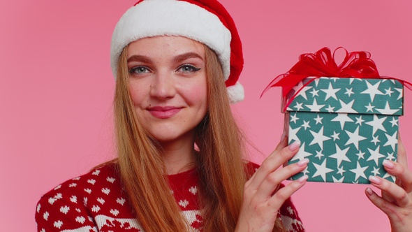 Cheerful Lovely Girl in Sweater Santa Hat Presenting One Christmas Box Excited By Holiday Gift alt