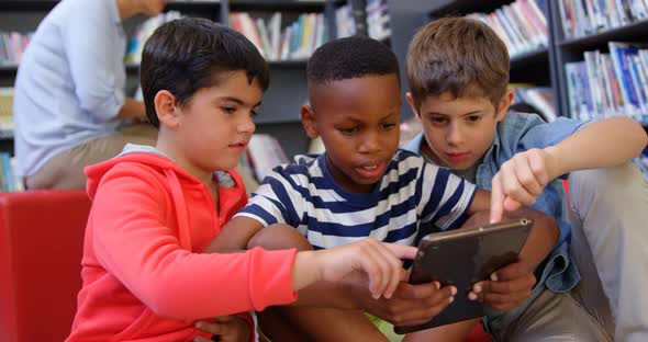 Front view of mixed-race schoolboys studying on digital tablet in the school library 4k alt