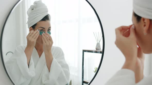 Beautiful Young Woman Applying Eye Patches Looking at Mirror in Bathroom and Smiling alt