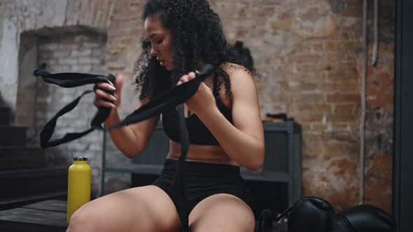 Exhausted Woman Takes Off Hand Wraps After Boxing Training alt