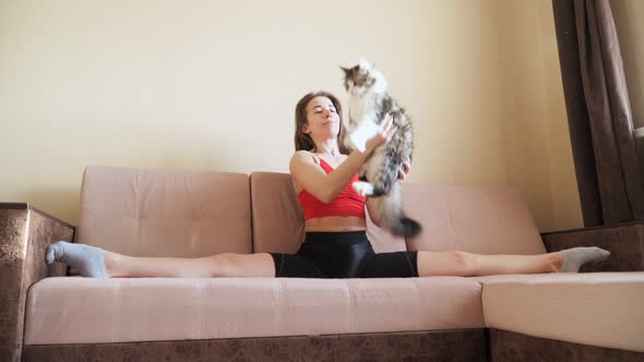 Young beautiful girl sitting in the splits on the bed and plays with the cat. Pastime home alt