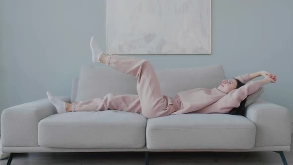 Young funny Caucasian woman with glasses resting lying on sofa in living room.