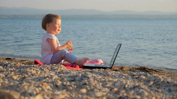 Baby Girl Sitting with Notebook on Seashore. New Generation of People Who Combine Work and Vacation
