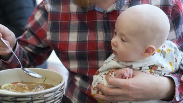 a man teases a baby son when he eats soup, brings a spoon but does not give