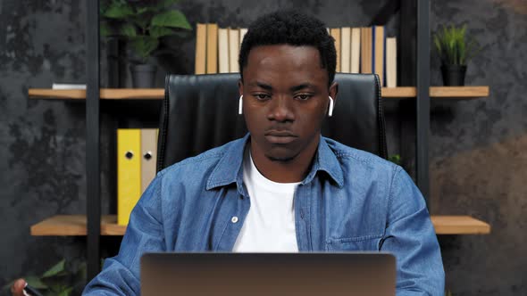 African American Man Works for Laptop in Office Writes Information in Notebook alt