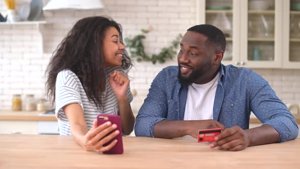 Happy Multiracial Couple Using a Smartphone for Shopping Online at Home alt