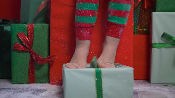 Child in a Green Dwarf Costume Sits on Gift Boxes with Deer Antlers alt