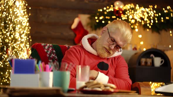 Santa Claus Boring. Tired Santa Claus Sleeping on the Table at Home alt