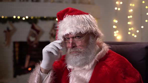 Portrait of an Offended Santa Claus in Glasses, Sitting in His Rocking Chair Near the Christmas Tree
