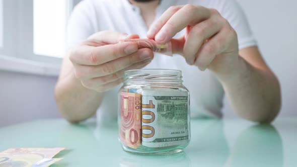 Close Up View of Male Hand Putting Pounds Banknote Into Glass Jar alt