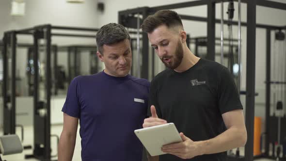 Handsome Professional Fitness Trainer with a Tablet in Hands Explaining the Plane of Training alt