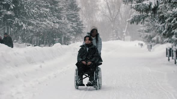Couple of Asian Guy in the Wheelchair and His Black Girlfriend Walking in Winter Park alt