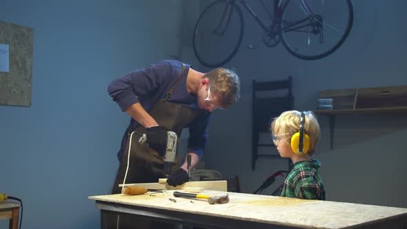 Boy Watches His Dad Drill a Board, Medium Long Shot alt