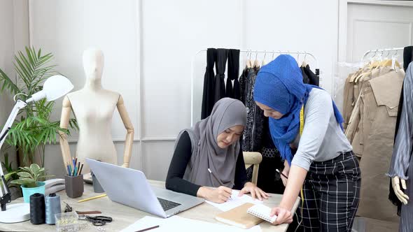 Muslim woman fashion designer team discussing dress sketch at the table in tailor shop