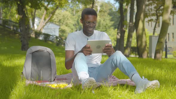Wide Shot of Carefree African American Man Watching Comedy Show on Tablet and Laughing. Portrait of alt