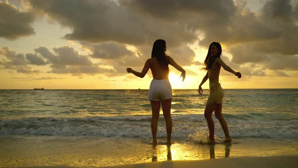 Two beautiful Asian women are having fun dancing on the beach at sunset on vacation, freedom concept