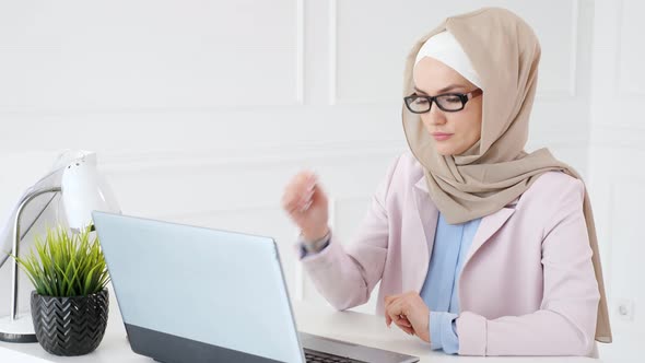 Tired Muslim Woman Works and Types on Laptop Puts Off Her Glasses and Rubs Her Eyes alt