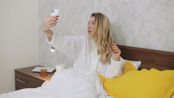 Woman Taking Selfie Photo and Video at Her Smartphone Front Camera in Bed alt