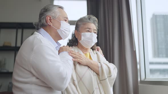 asian retired elderly couple wearing face masks watch the world through their home window