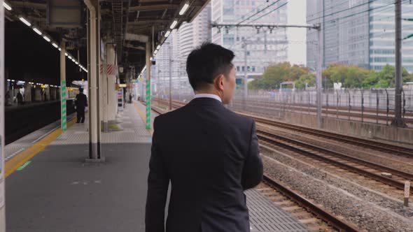 Japanese businessman waiting on a train platform alt