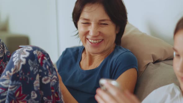 Smiling mother looking at her daughters phone alt