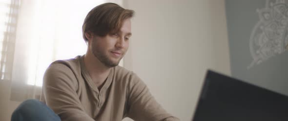A close up of a young man sitting in bed and working on a computer.  alt