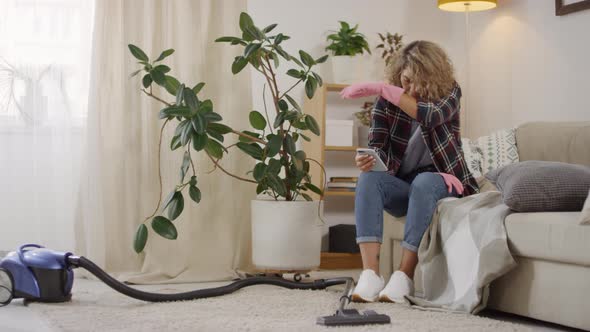 Woman Sitting on Couch with Mobile Phone after Cleaning Apartment alt