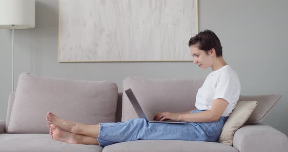 Side View of Student Sitting at Sofa Typing on Laptop at Home Background