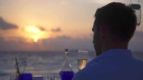 A man and woman couple dine and drink champagne on a tropical island beach alt