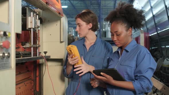 Two professional female engineers inspect machines' electric systems at factory.