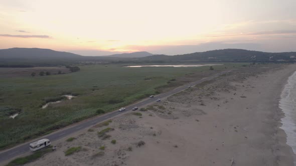 Aerial View of Coastal Road with Low Traffic Against Sunrise Above Green Hills alt