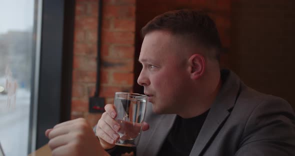 The Man Drinks A Glass Of Clean Water And Looks Out The Window