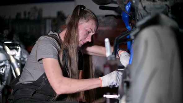 Young woman with a dirty face repairs a motorcycle in a motorcycle service alt