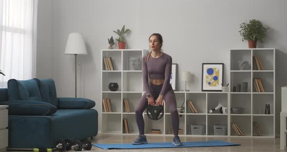Squats with Weight Woman Is Training at Home in Living Room Fulllength Shot in Modern Interior alt