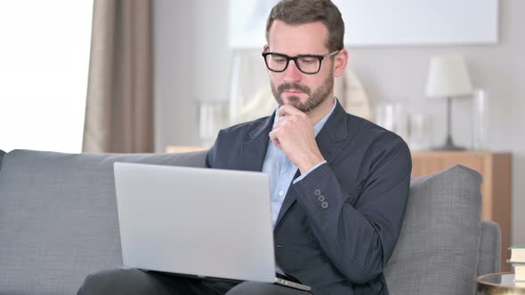 Pensive Young Businessman Using Laptop at Home  alt