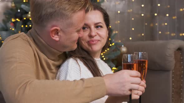 Couple in Love Sitting and Hugging Near the Christmas Tree and Drinking Champagne alt