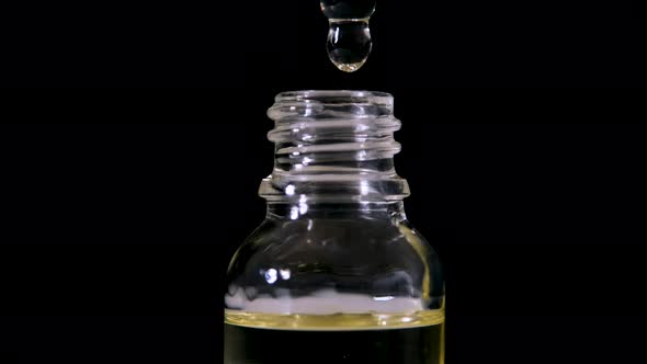 Drop Falls From a Pipette in a Medical Bottle Closeup Isolated on a Black Background