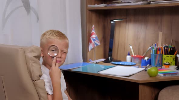 Portrait of a Boy at Home at the Table He is Playing with a Magnifying Glass alt