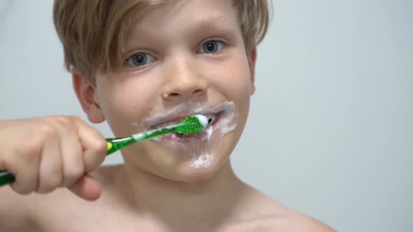 Cheerful Little Boy Brushing Teeth in Front of the Bathroom Mirror