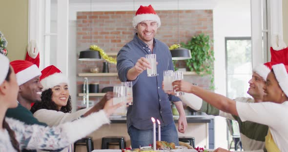 Happy group of diverse friends in santa hats celebrating meal, toasting with juice at christmas time alt