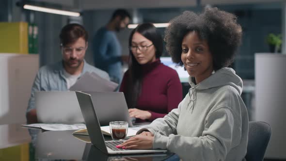Portrait of AfricanAmerican Woman Working on Laptop and Smiling at Camera in Office alt