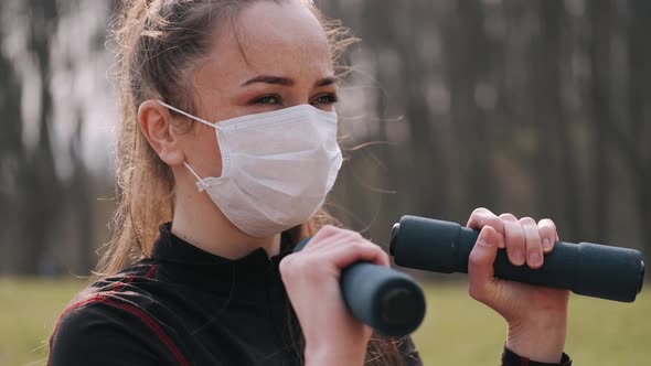 Athletic Woman in a Protective Mask Is Doing Exercise with Dumbbells alt