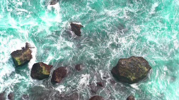 Aerial view 4k waves break on dark rocks near beach. Sea waves on the stones