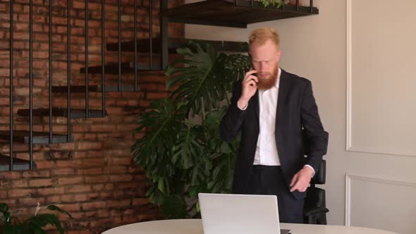 Redhaired Bearded Modern Businessman in Formal Suit Talking on the Smartphone