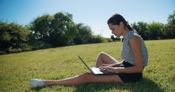 Freelance Woman Working with Laptop and Receiving Mobile Phone Call Outdoors alt